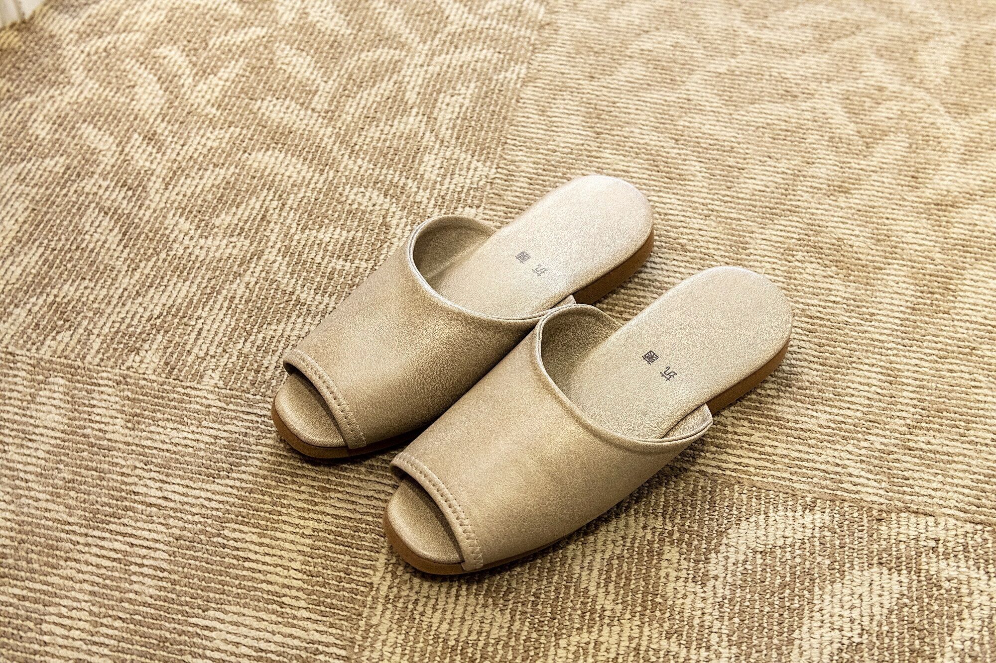 A pair of beige slippers on a textured beige carpet.