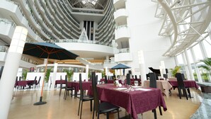 A multi-level atrium with dining tables, chairs, and umbrellas, featuring a central glass ceiling and white structural elements. - Hotel Kyocera (Kirishima)
