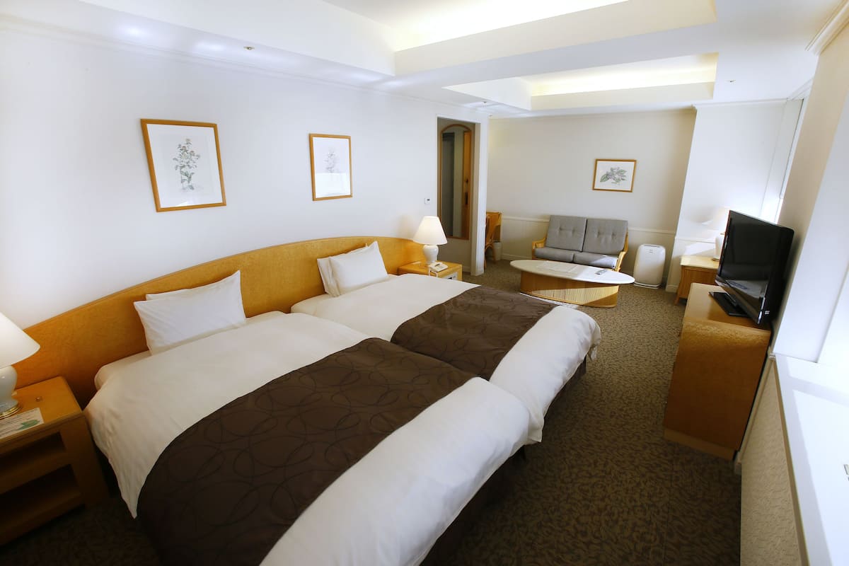 A hotel room with two beds, a TV, a desk, and a chair.