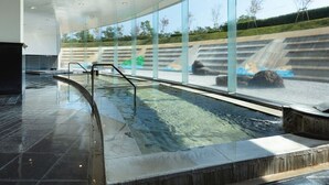 A modern indoor pool with glass walls, a clear view of the outdoors, and a waterfall feature. - Hotel Kyocera (Kirishima)