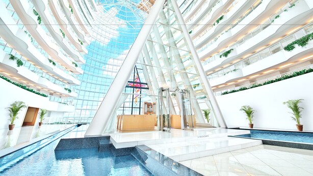A modern atrium with a glass ceiling, multiple floors, and a central water feature. - Hotel Kyocera (Kirishima)