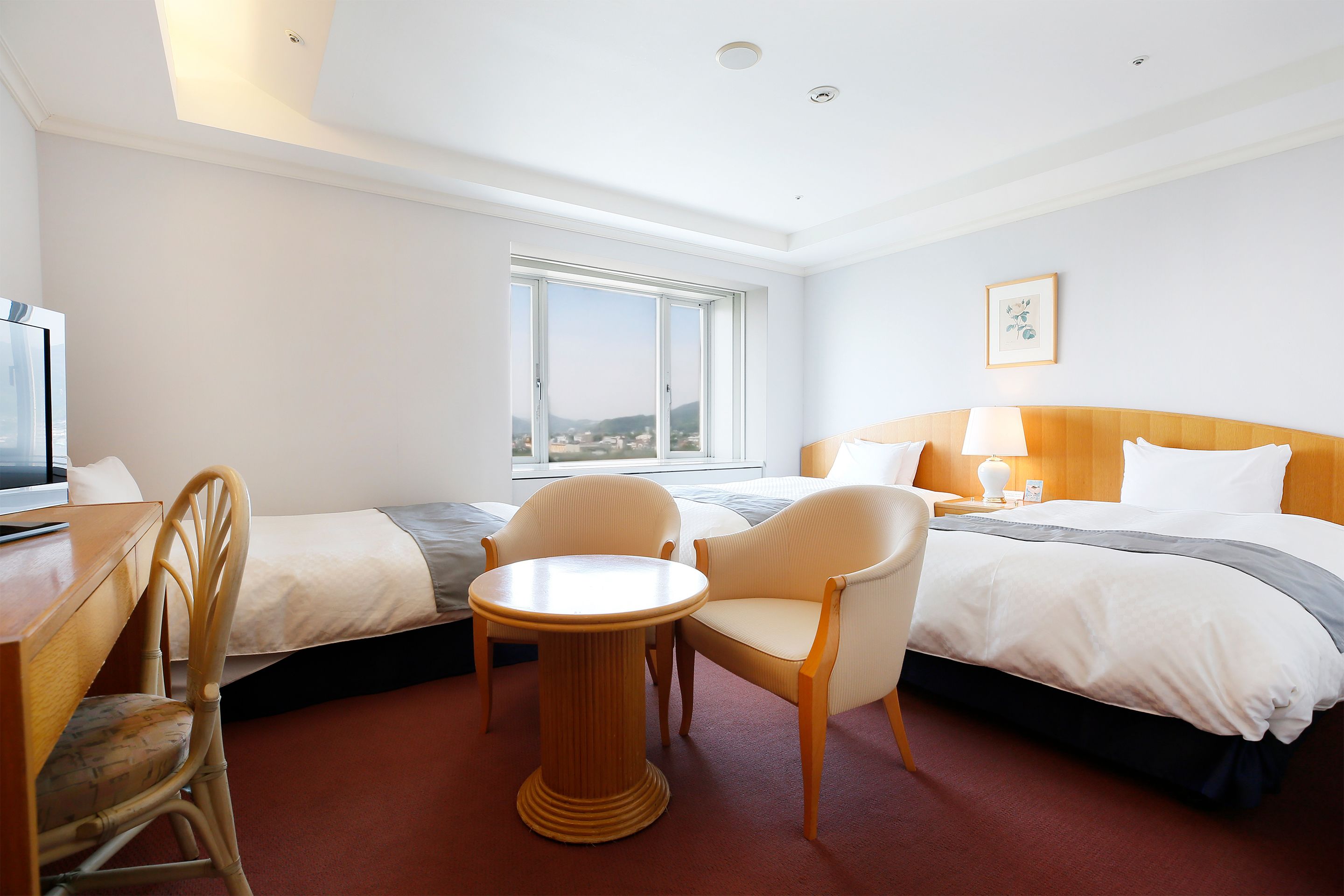A hotel room with two beds, a desk, a chair, and a small table.