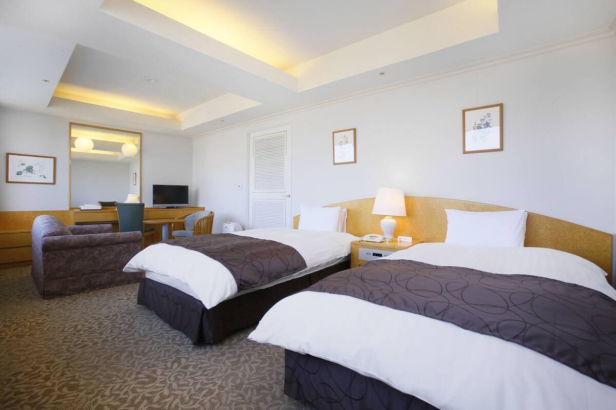 A hotel room with two beds, a desk, a chair, a TV, and a mirror.