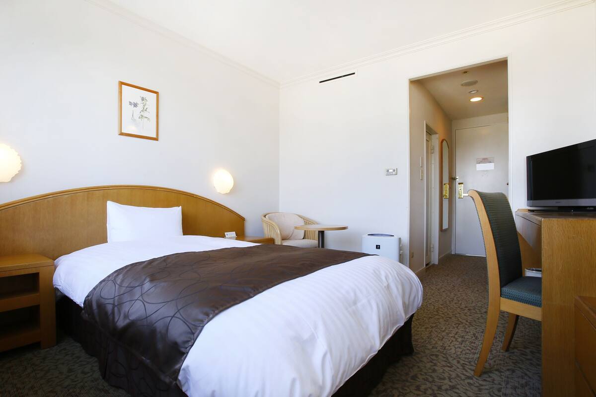 A hotel room with a bed, bedside table, chair, desk, television, and a framed picture on the wall.