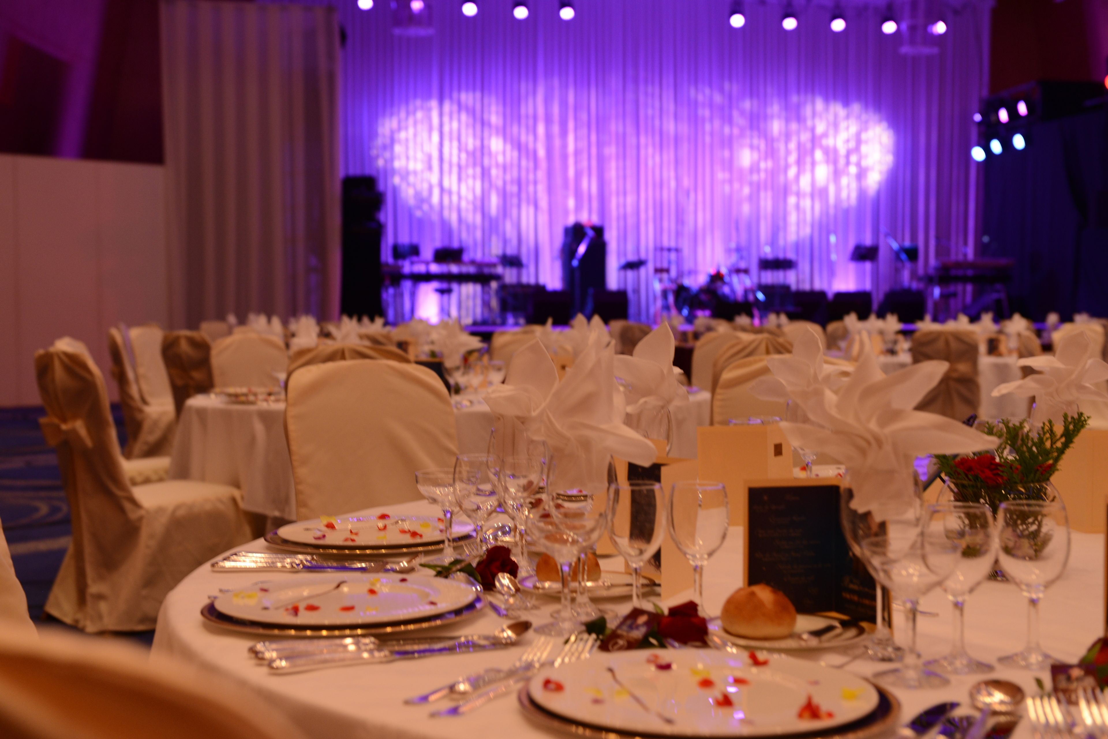 A banquet hall with round tables set for a formal event, complete with white tablecloths, fine china, and glassware.