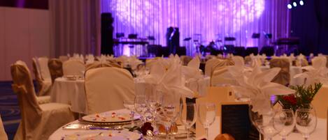 A banquet hall with round tables set for a formal event, complete with white tablecloths, fine china, and glassware.