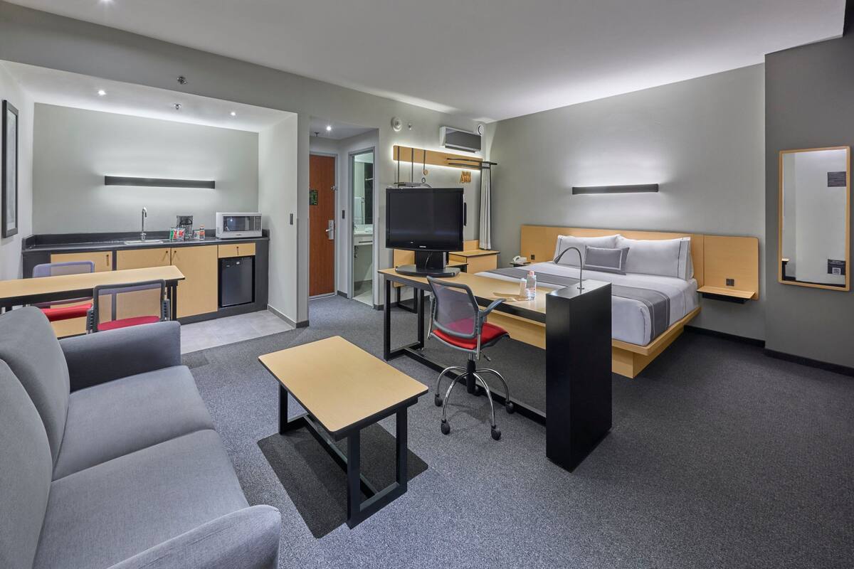 A modern hotel room with a sofa, desk, and bed.