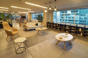 Un moderno vestíbulo de hotel con un sofá, sillones, una mesa de centro y una estantería.