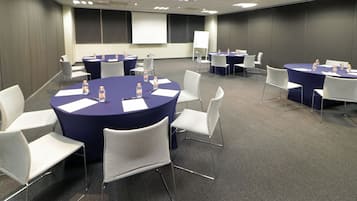 A conference room with round tables, white chairs, and a projector screen.