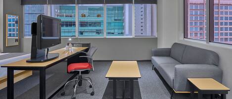 Un espacio de oficina moderno con un escritorio, computadora y un sofá gris.