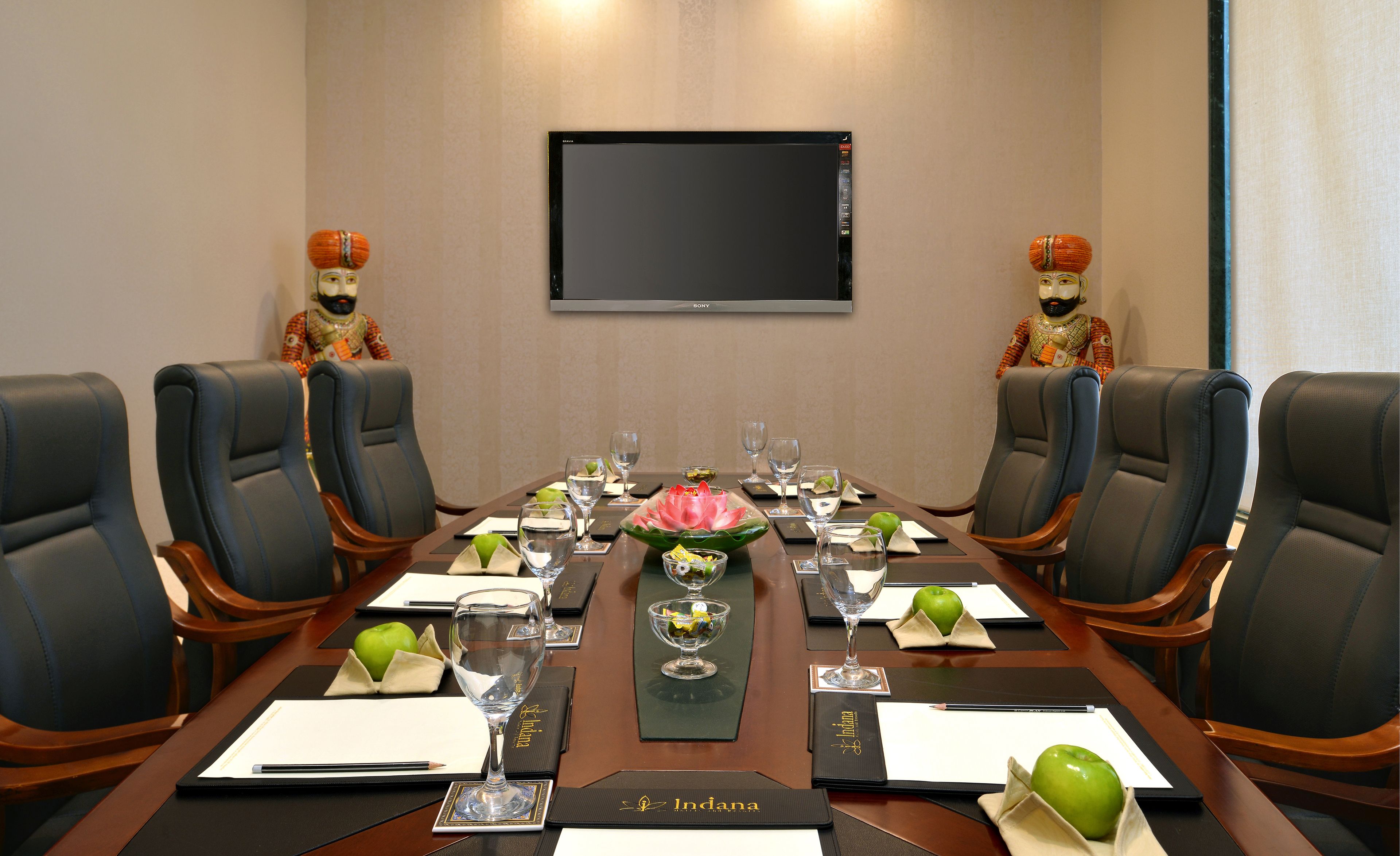 A conference room with a long table, black leather chairs, a large screen, and decorative figurines.
