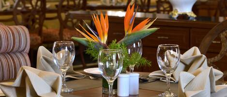 Una mesa de comedor puesta con servilletas dobladas, copas de vino y un centro de mesa con flores de ave del paraíso.