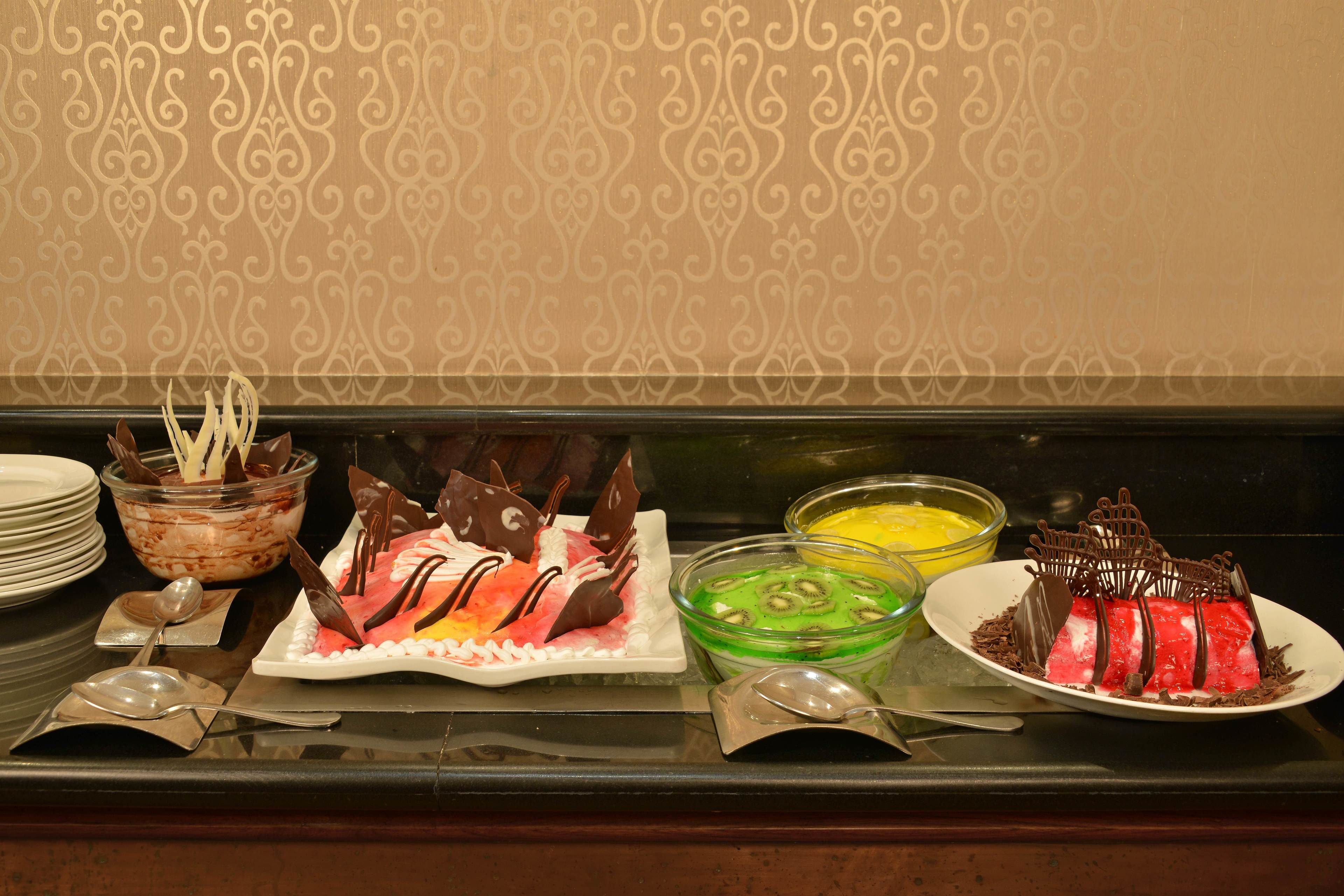 A buffet table with various desserts and a patterned wallpaper background.