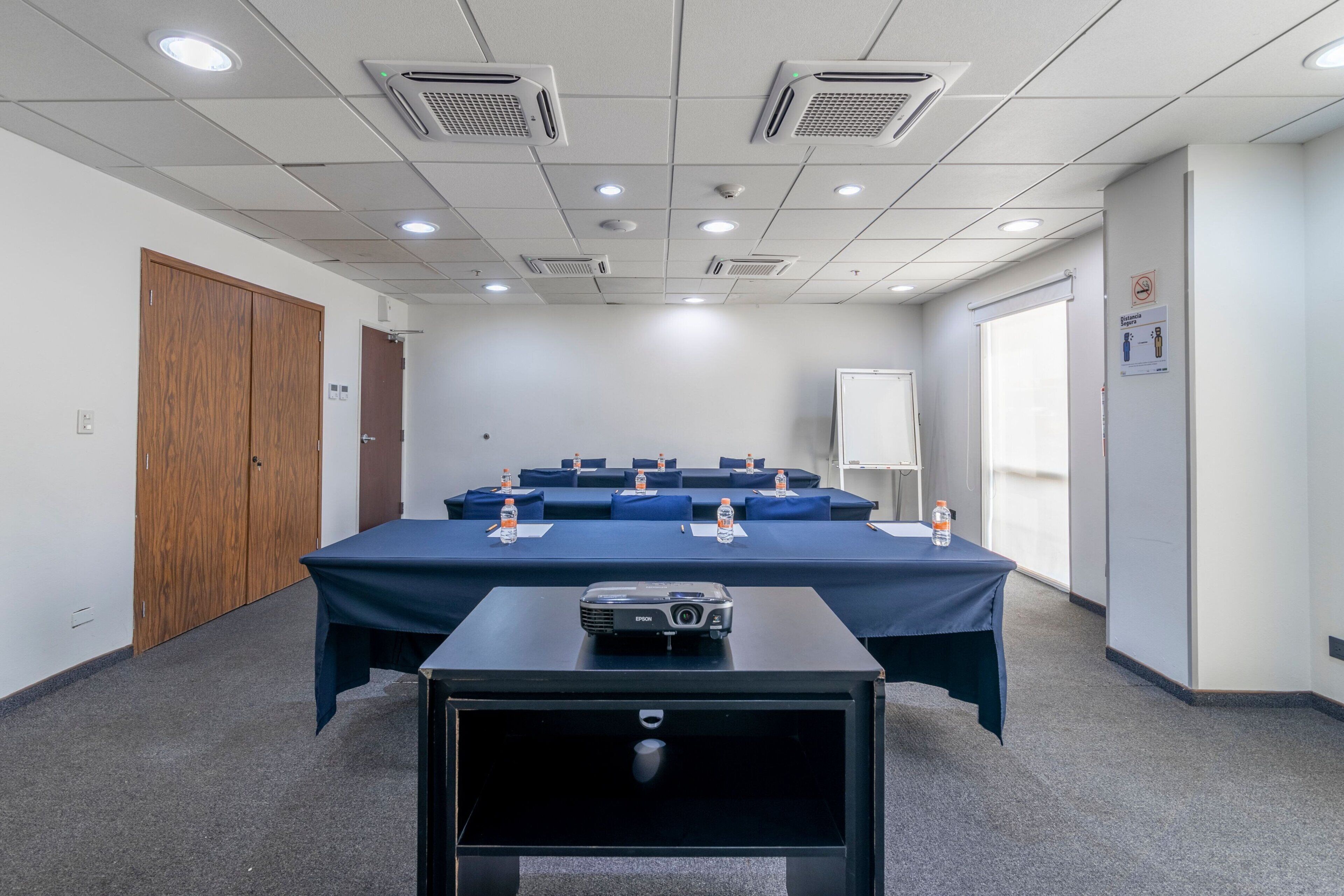 A conference room with a long table, blue chairs, a projector, and water bottles.