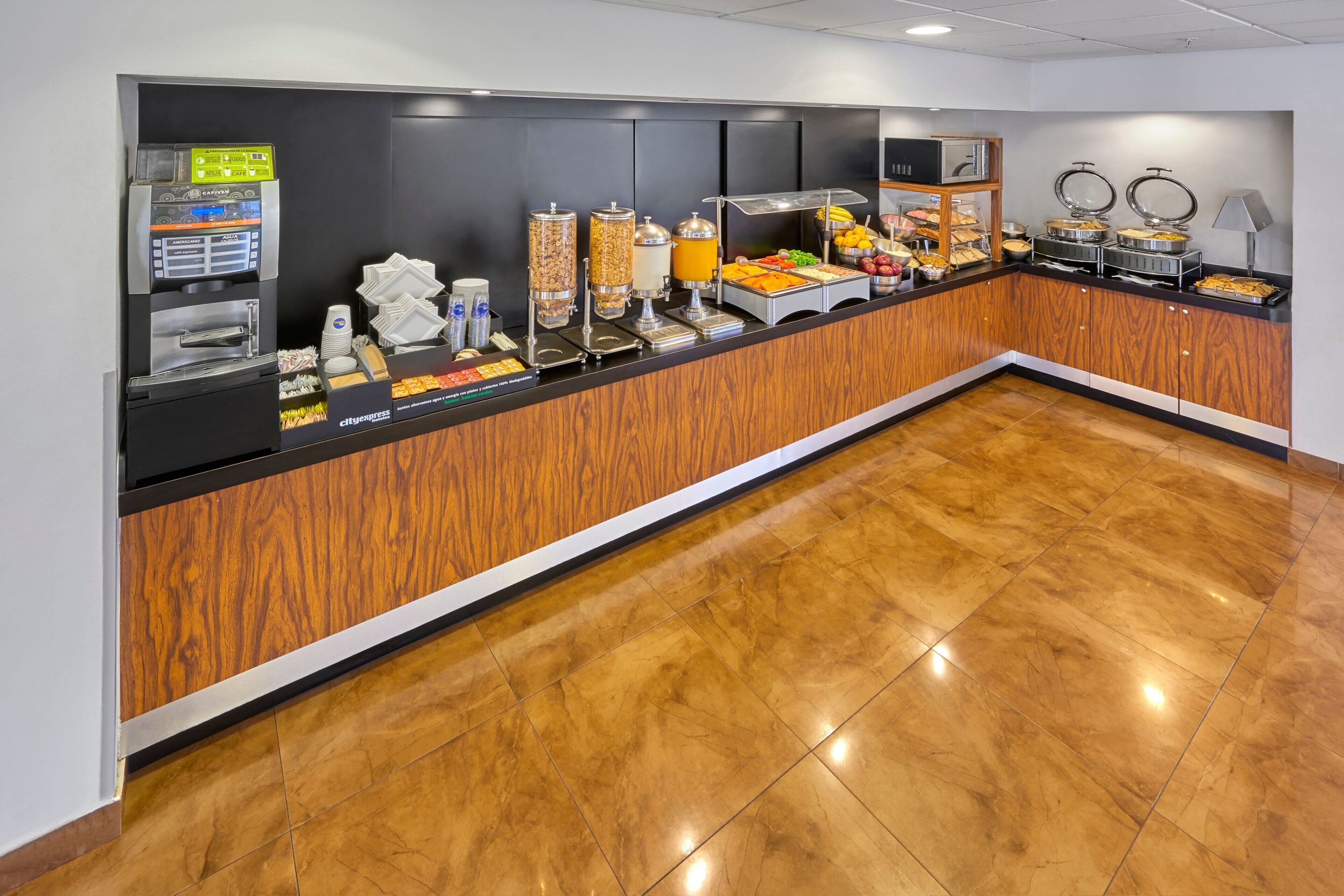 A buffet counter with a coffee machine, juice dispenser, and various food items.