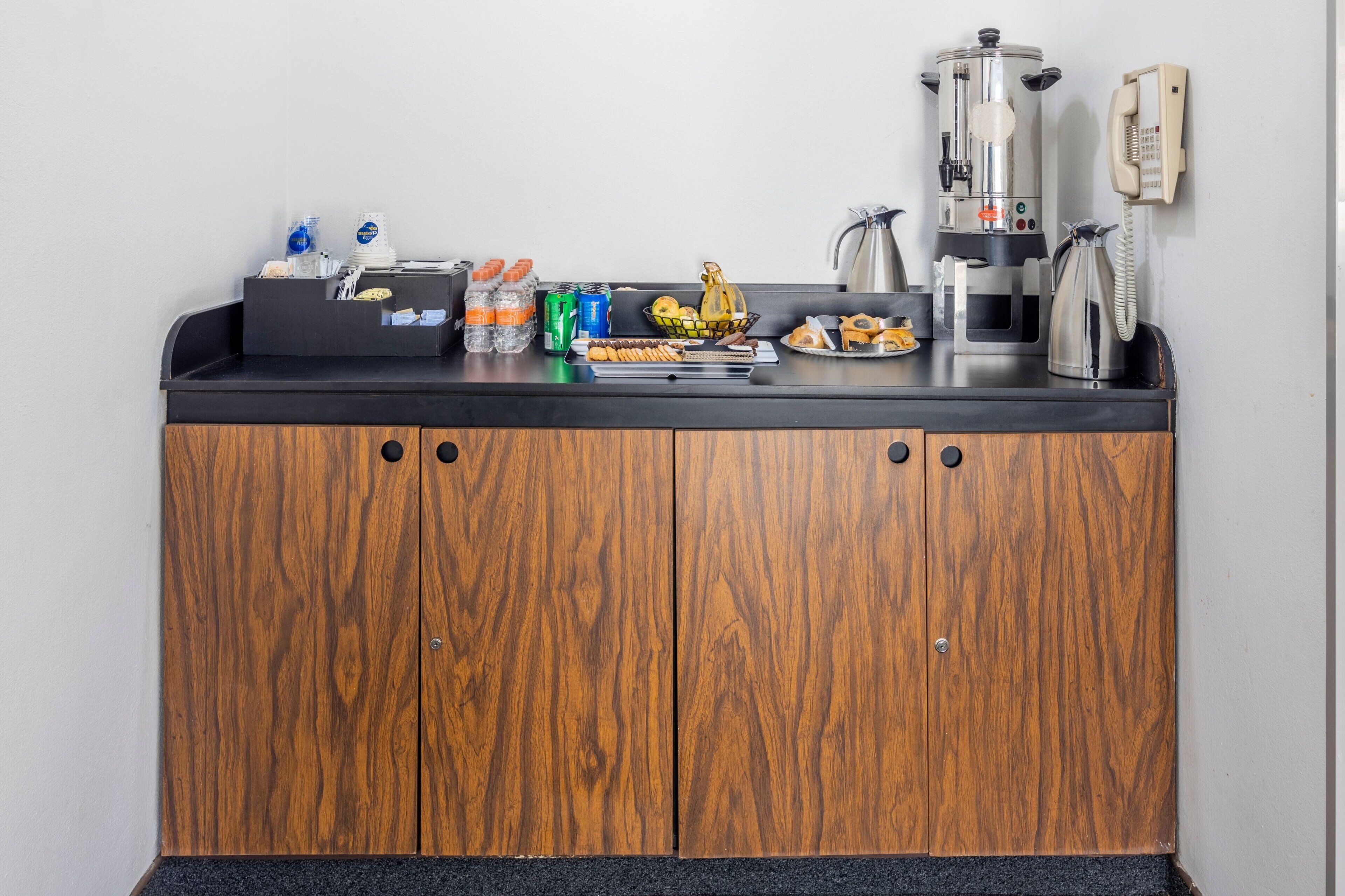 A kitchenette with a coffee maker, a kettle, and various food items on the counter.