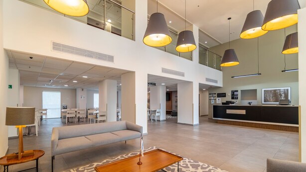 A spacious lobby with a reception desk, a grey sofa, a wooden coffee table, and pendant lighting. - City Express by Marriott Chetumal (Chetumal)