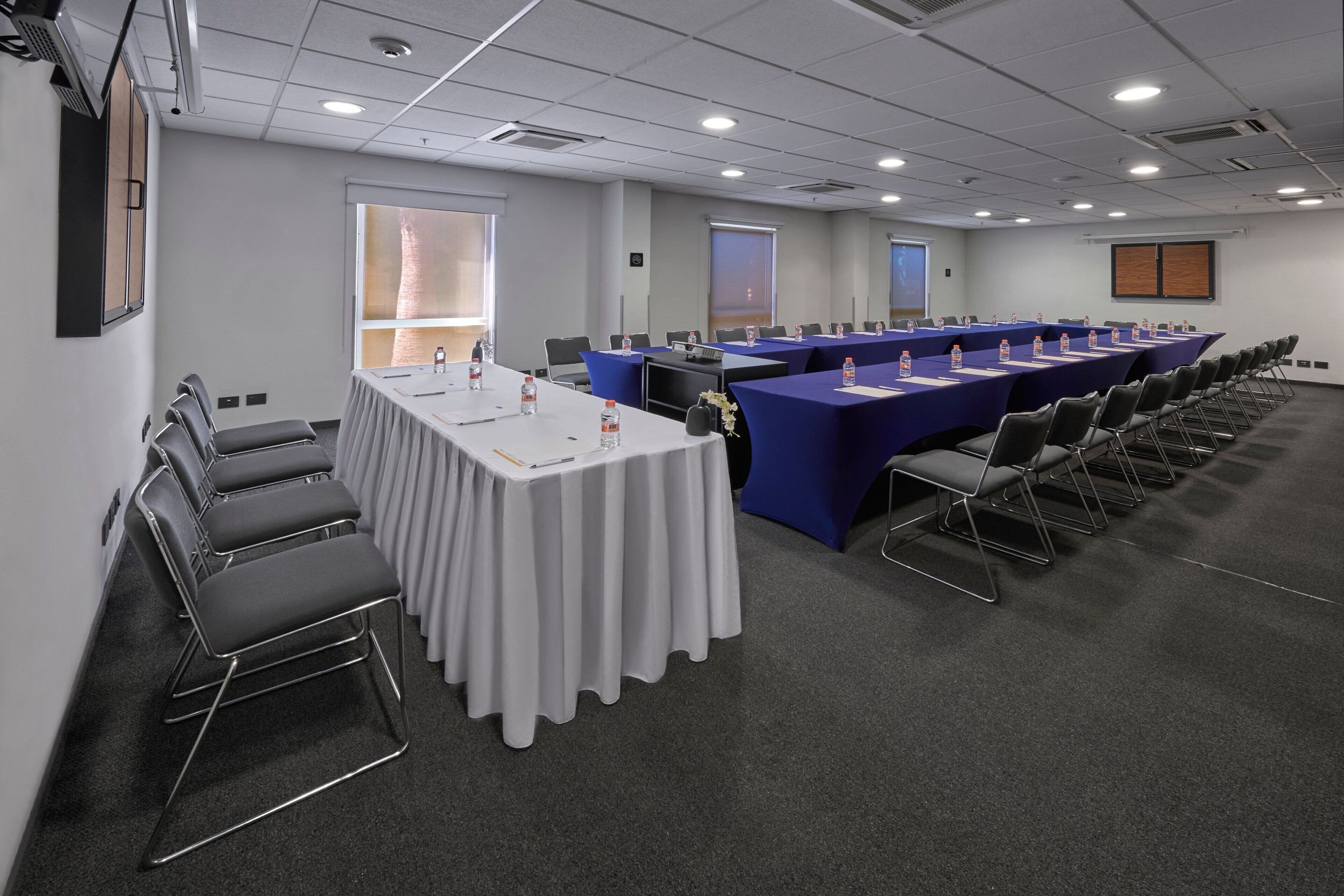 Un salón de conferencias con una larga mesa, sillas y una pantalla de proyector.