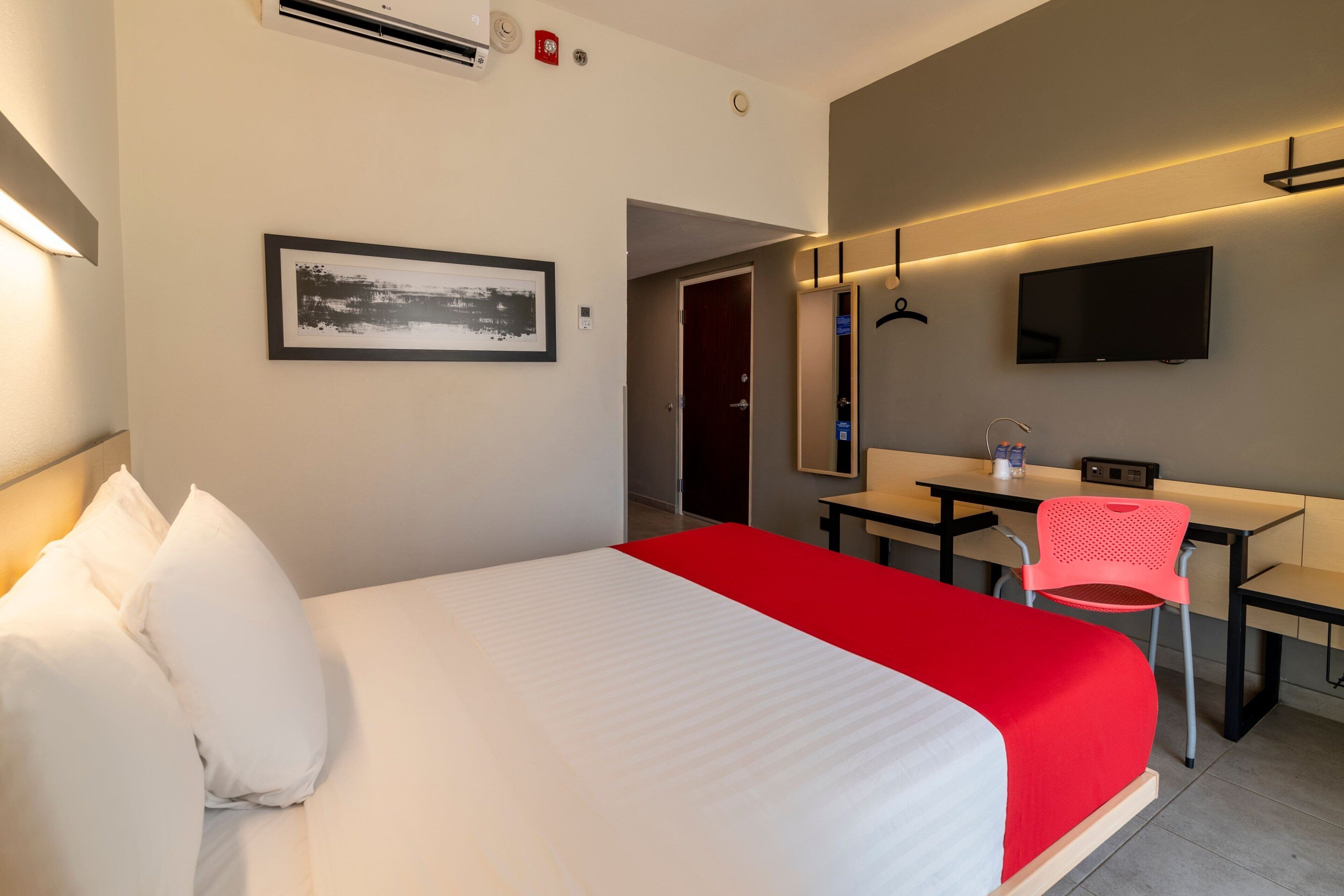 Habitación de hotel con cama, escritorio, silla, televisor y un cuadro en la pared.