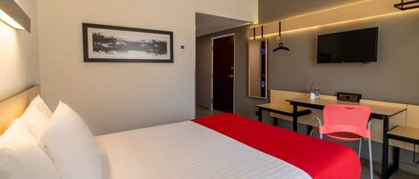 Habitación de hotel con cama, escritorio, silla, televisor y un cuadro en la pared.