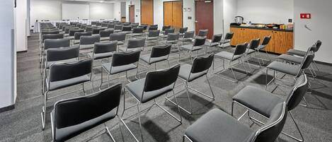 A conference room with rows of chairs, a podium, and a kitchenette area.