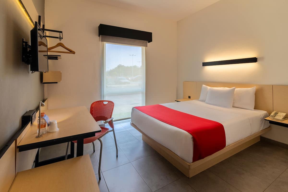 Habitación de hotel con cama, escritorio, silla, teléfono y ventana con vistas al exterior.