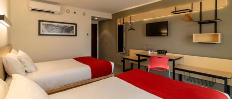 Une chambre d’hôtel avec deux lits, un bureau, une chaise, une télévision et un climatiseur fixé au mur.