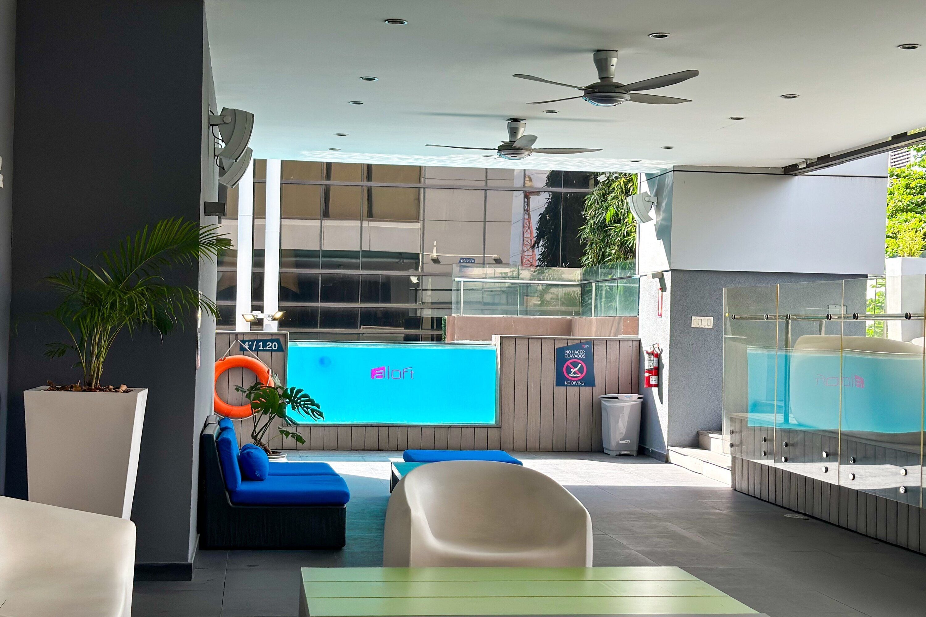 A modern outdoor seating area with blue cushions, a pool, and a glass enclosure.