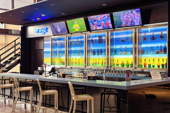A bar area with multiple screens displaying sports events, a bar counter with stools, and a variety of bottles behind glass.