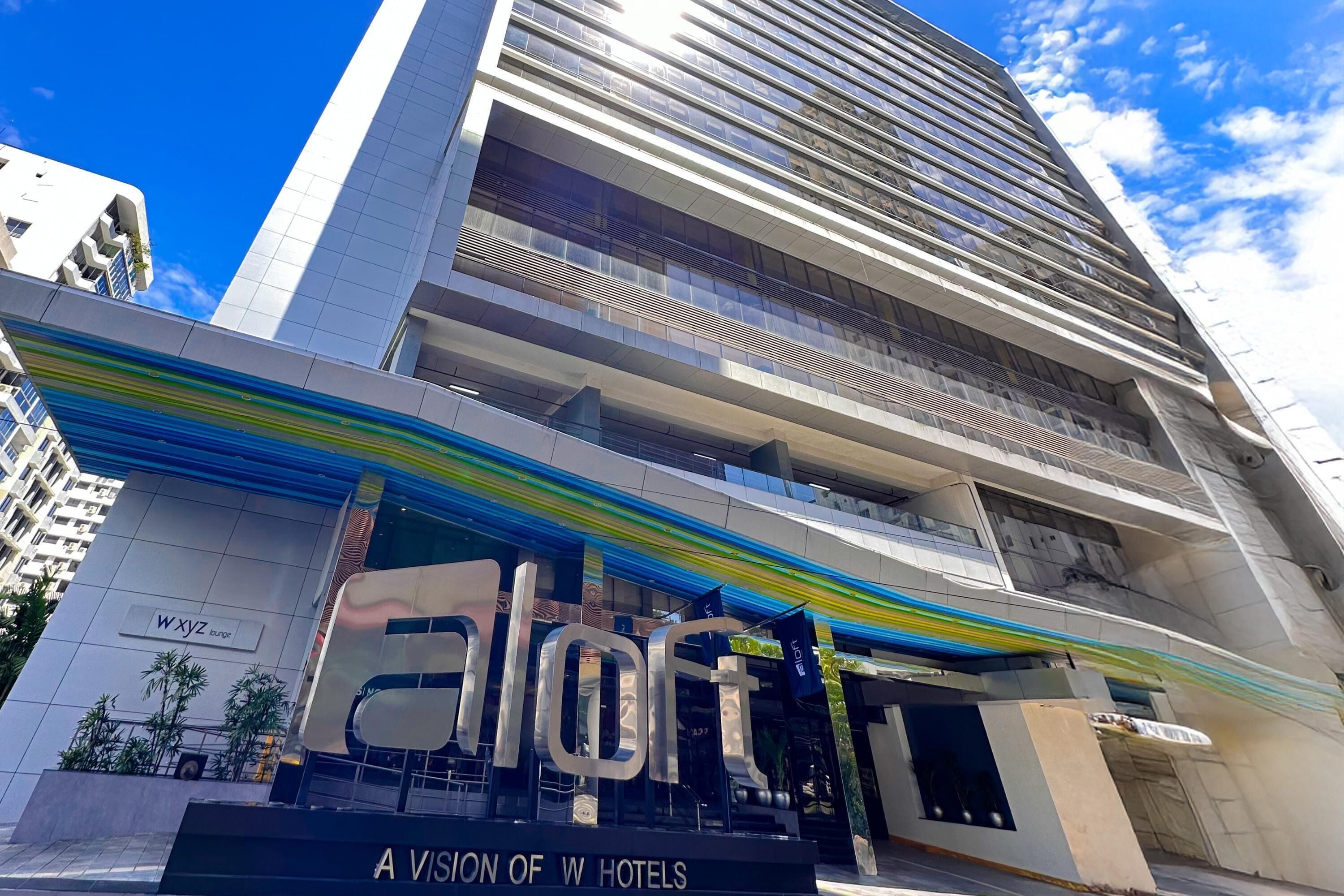 A modern hotel with a prominent 'aloft' sign, a view of WXYZ, and a clear blue sky.