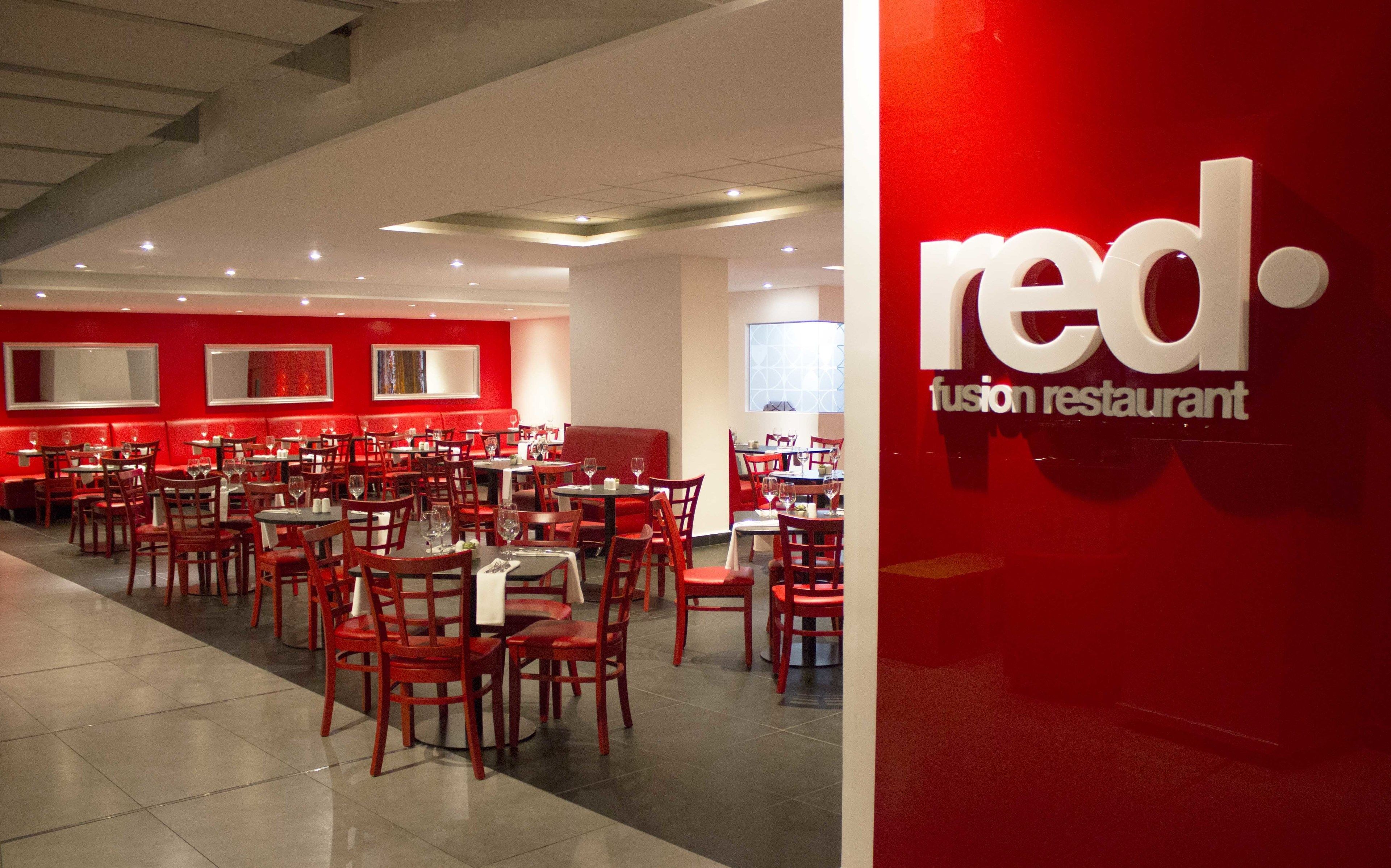 Un restaurante de cocina fusión roja con varias mesas y sillas rojas, que presenta una decoración de interiores moderna.