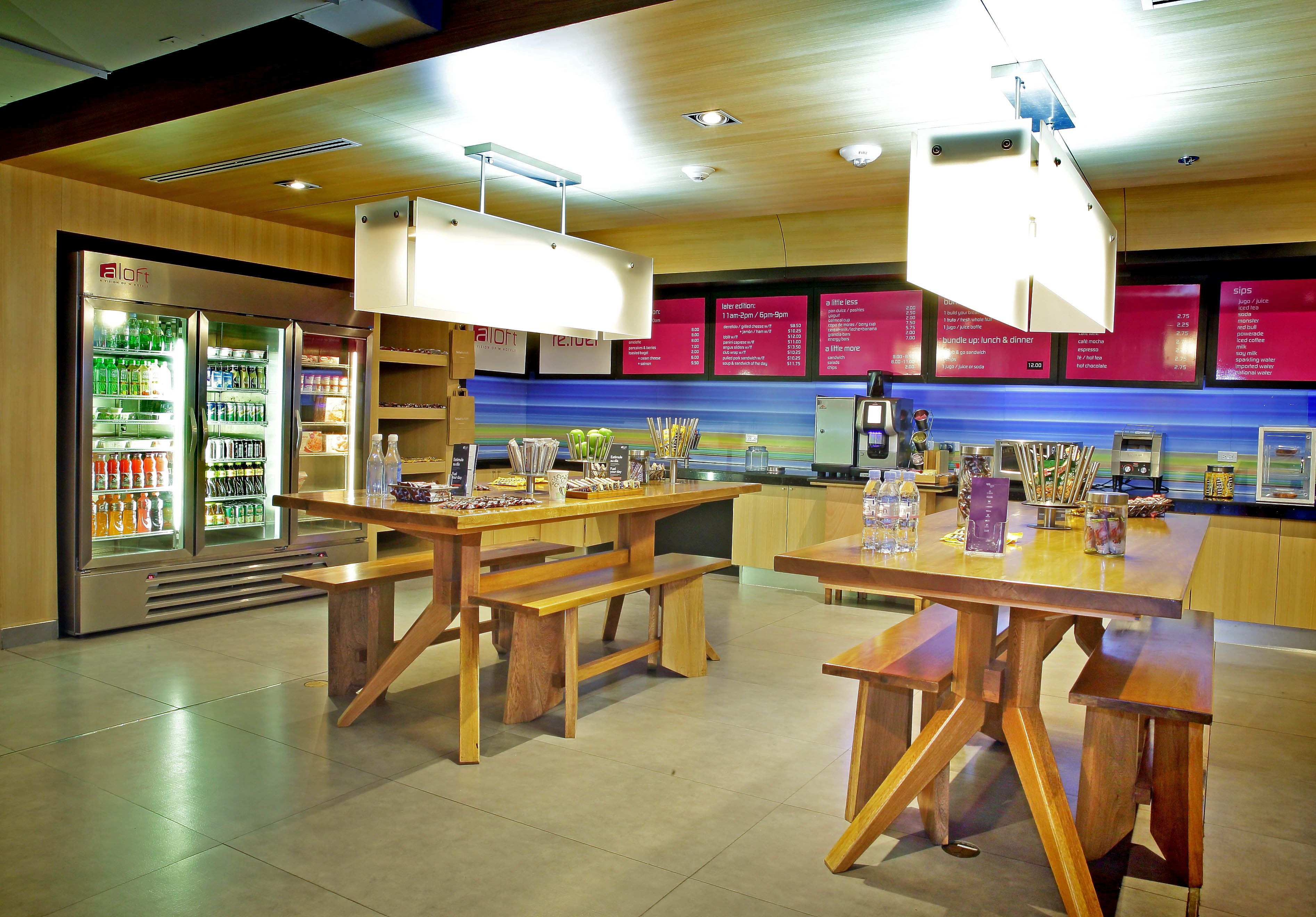 Ein modernes Restaurant mit Holztischen und -bänken, einer gekühlten Getränkeauslage und Speisekartenaushängen an der Wand.