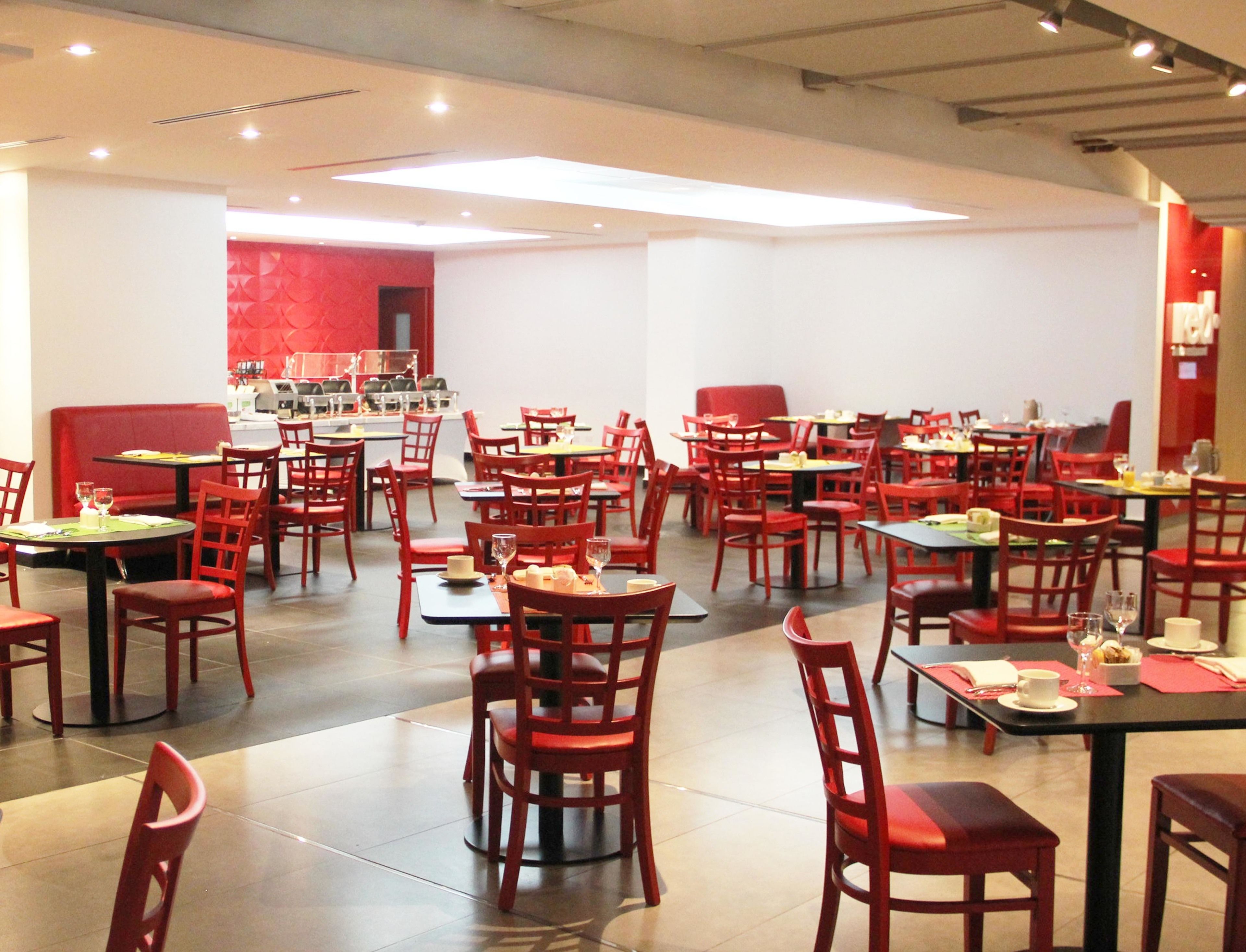 A restaurant with red chairs and tables, a red booth, and a white wall with a red pattern.
