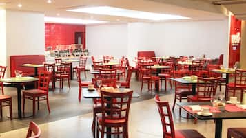 A restaurant with red chairs and tables, a red booth, and a white wall with a red pattern.