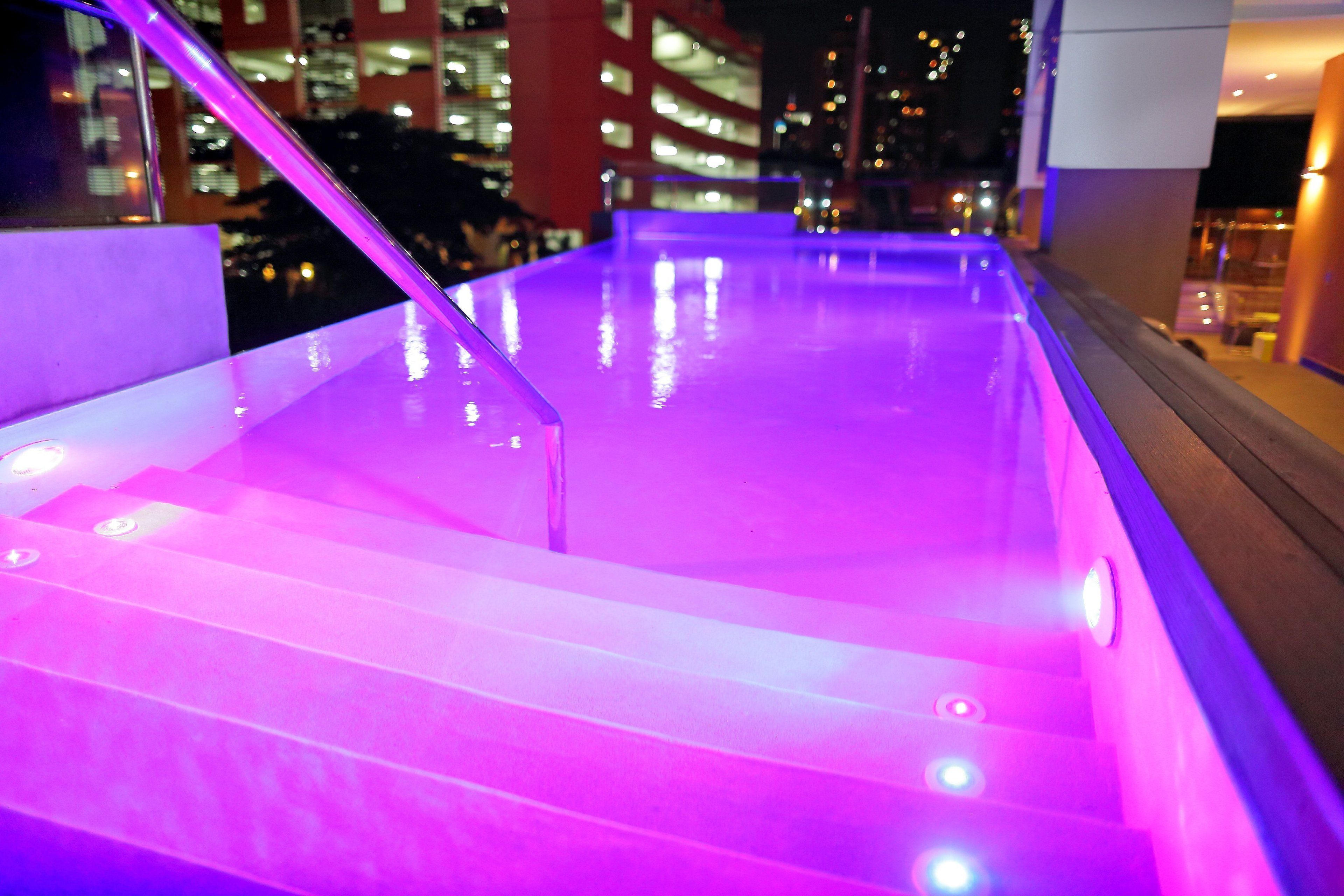 Un área de piscina interior moderna con una barandilla de vidrio e iluminación morada.