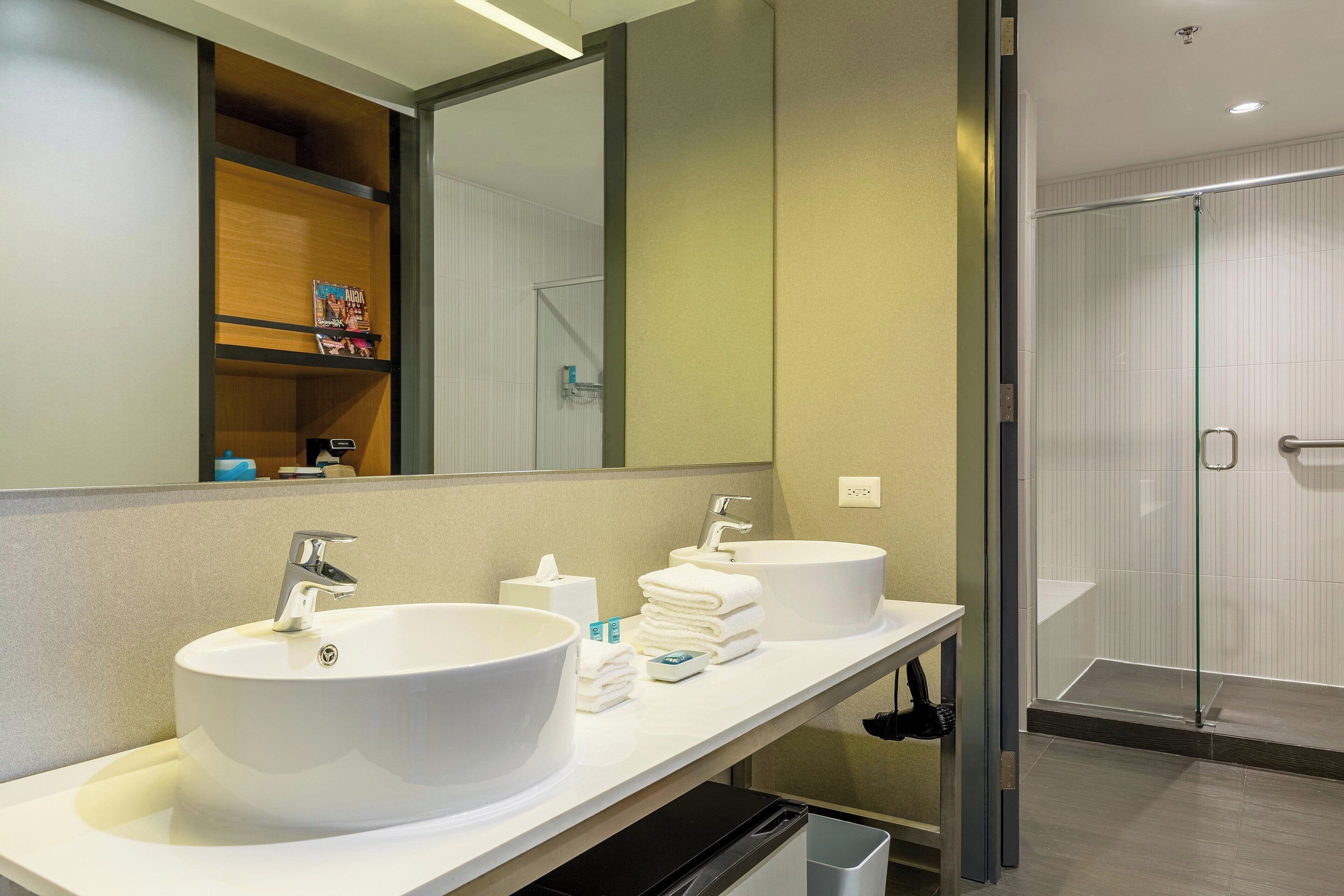 A modern bathroom with two large white sinks, a mirror, and a glass shower enclosure.