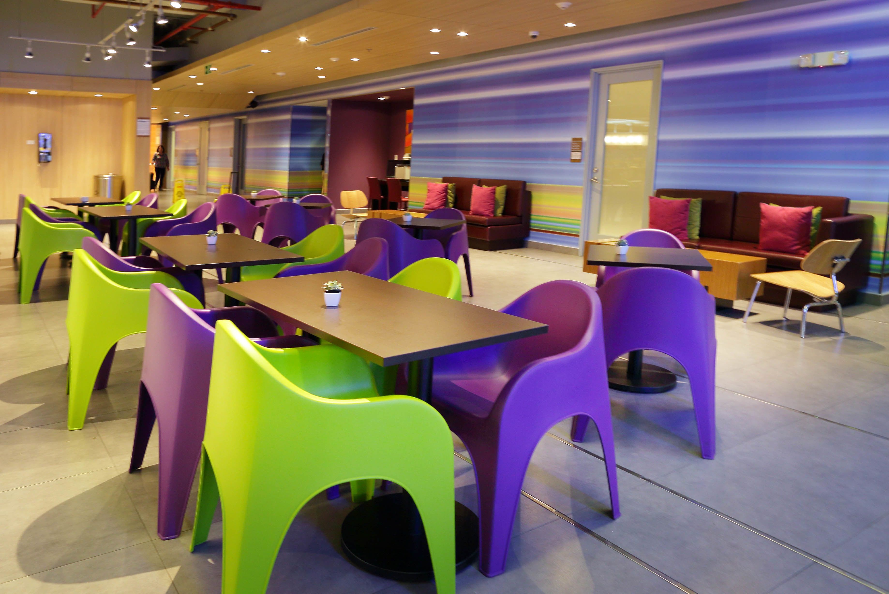 A modern dining area with vibrant chairs and tables, a seating area with couches, and a large window with a view.