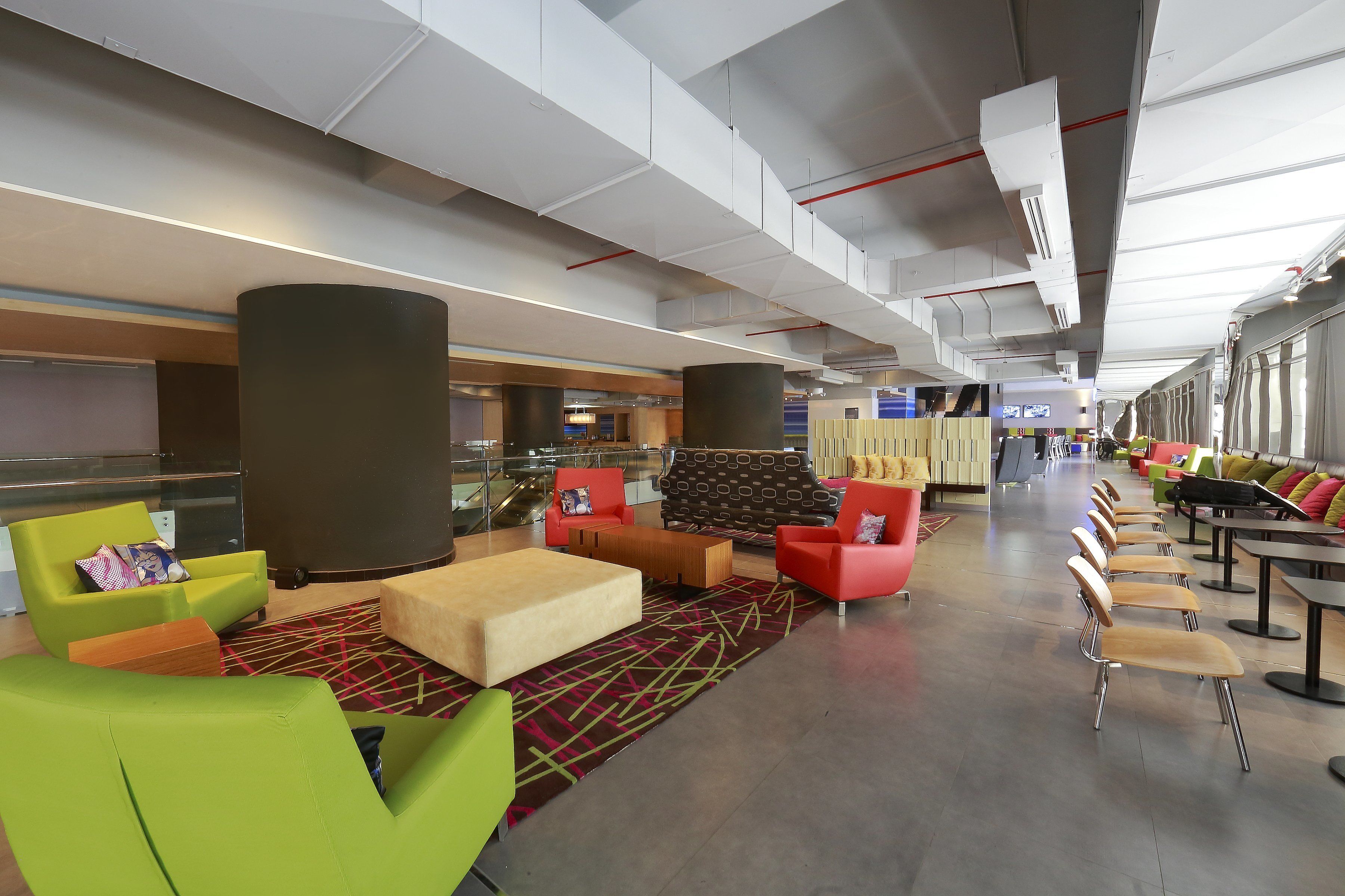 Un espace lounge moderne, doté de différents types de sièges, d’une colonne centrale et offrant une vue sur le terminal de l’aéroport en arrière-plan.