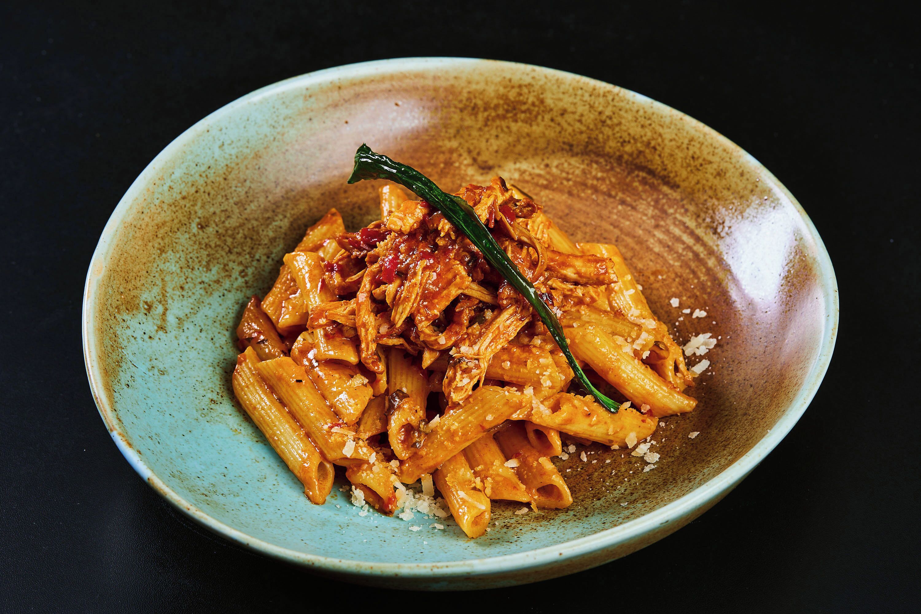 Un plato de pasta con un chile verde como adorno, sobre un plato de cerámica con motas.