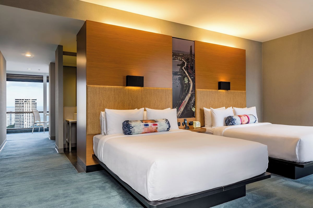 A modern hotel room with two beds, a large cityscape artwork on the wall, and a balcony with a view of buildings.