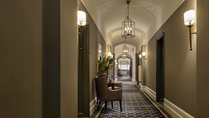 A hallway with a chandelier, wall sconces, a potted plant, and a chair.