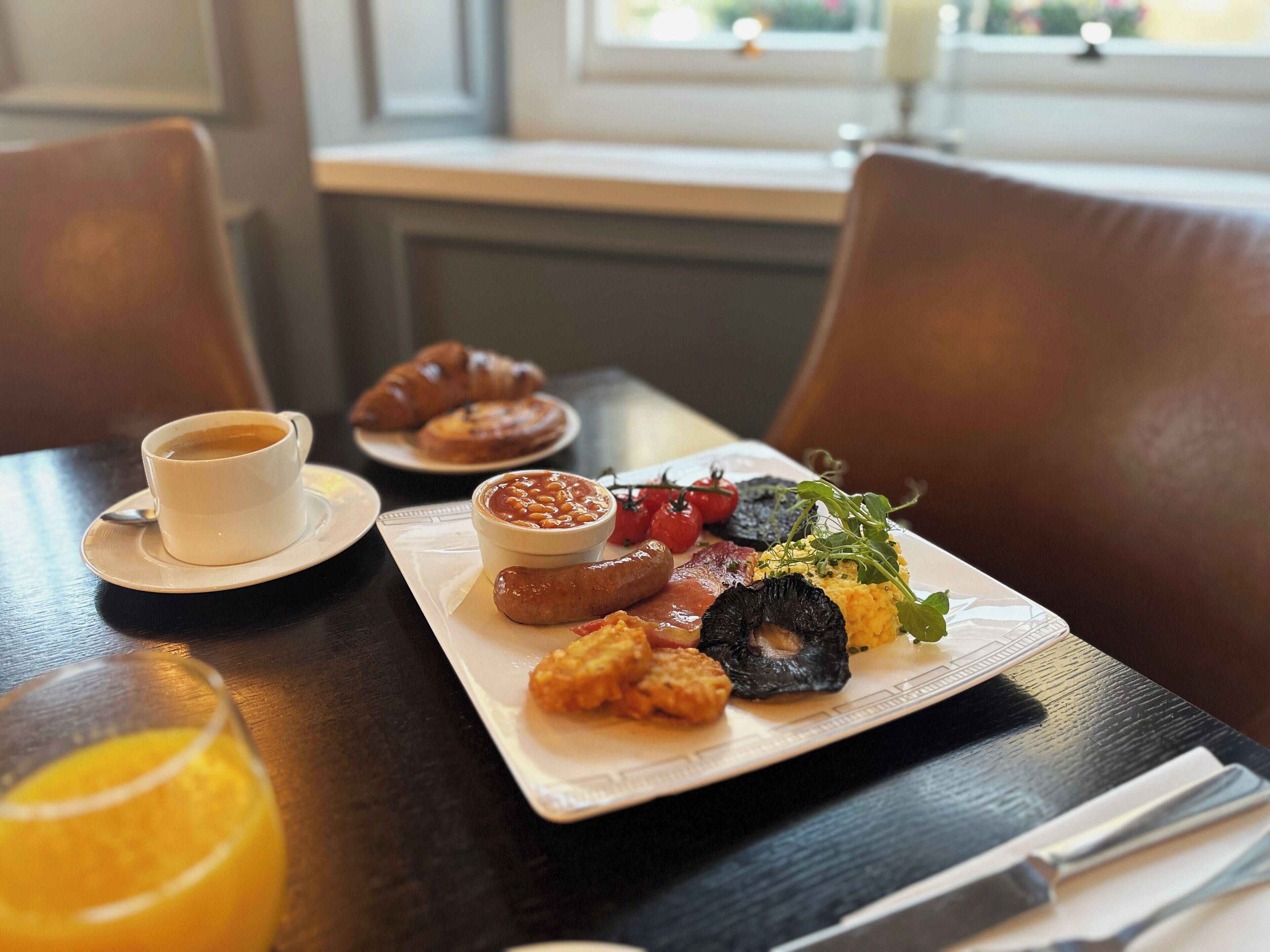 A breakfast tray with croissants, beans, tomatoes, and a variety of meats on a table.