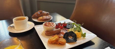 A breakfast tray with croissants, beans, tomatoes, and a variety of meats on a table.