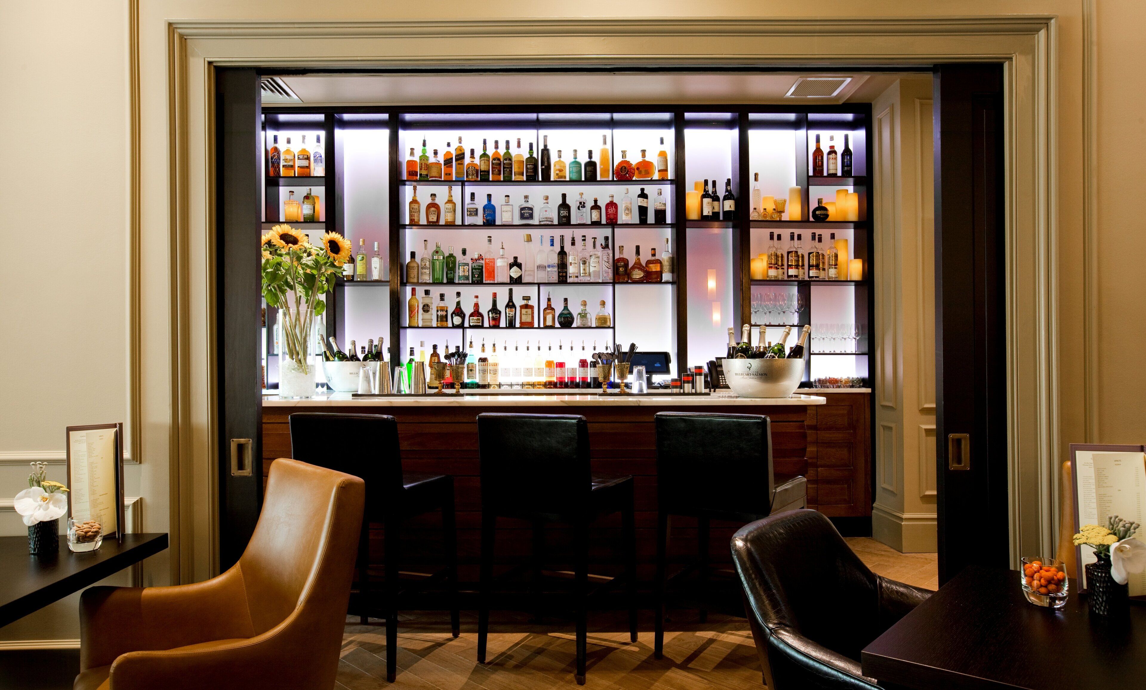 Un espace bar doté de plusieurs étagères remplies de bouteilles d’alcool, d’un comptoir et de fauteuils en cuir.