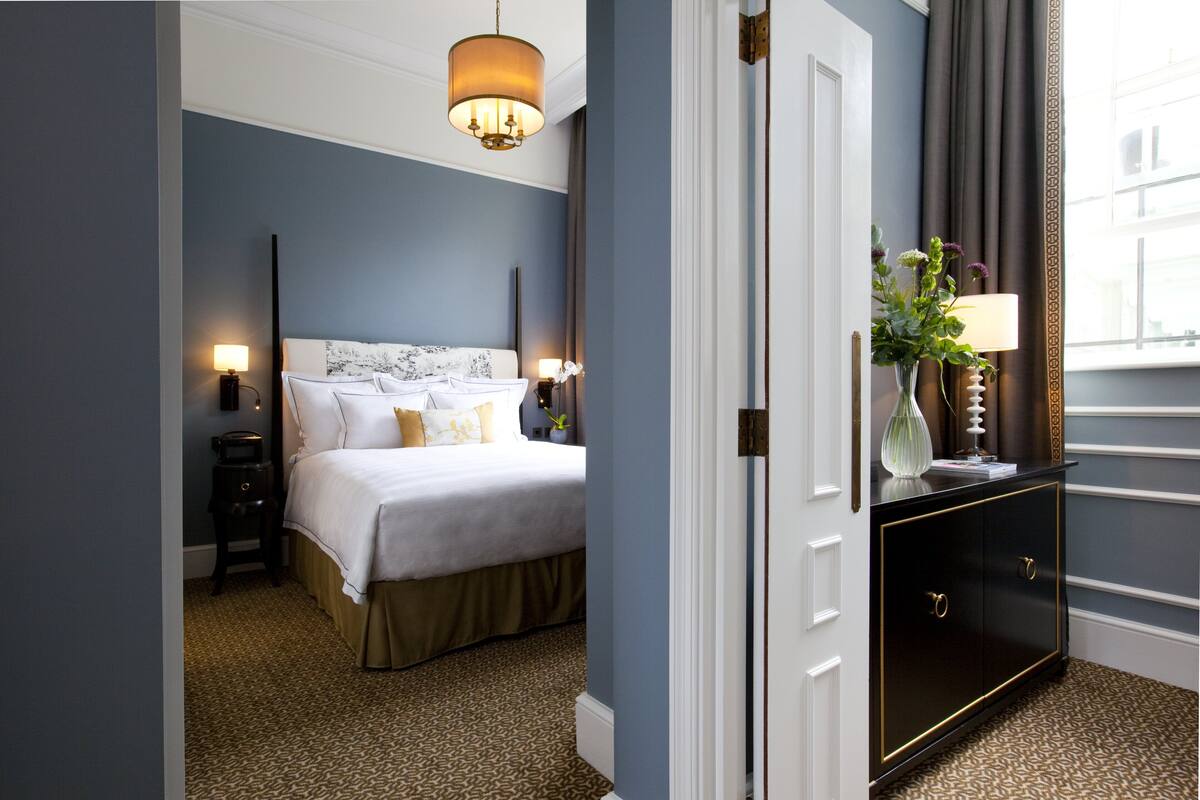 Ein Hotelzimmer mit einem großen Bett, zwei Nachttischlampen, einem Nachttisch, einer Kommode und einem Fenster mit Vorhängen.