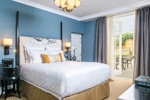 A hotel room with a large bed, two bedside lamps, a nightstand, a small table, and a view of the outdoor patio.