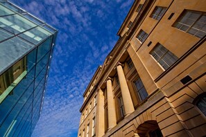 A modern glass building adjacent to a classical stone building with columns and arched windows.