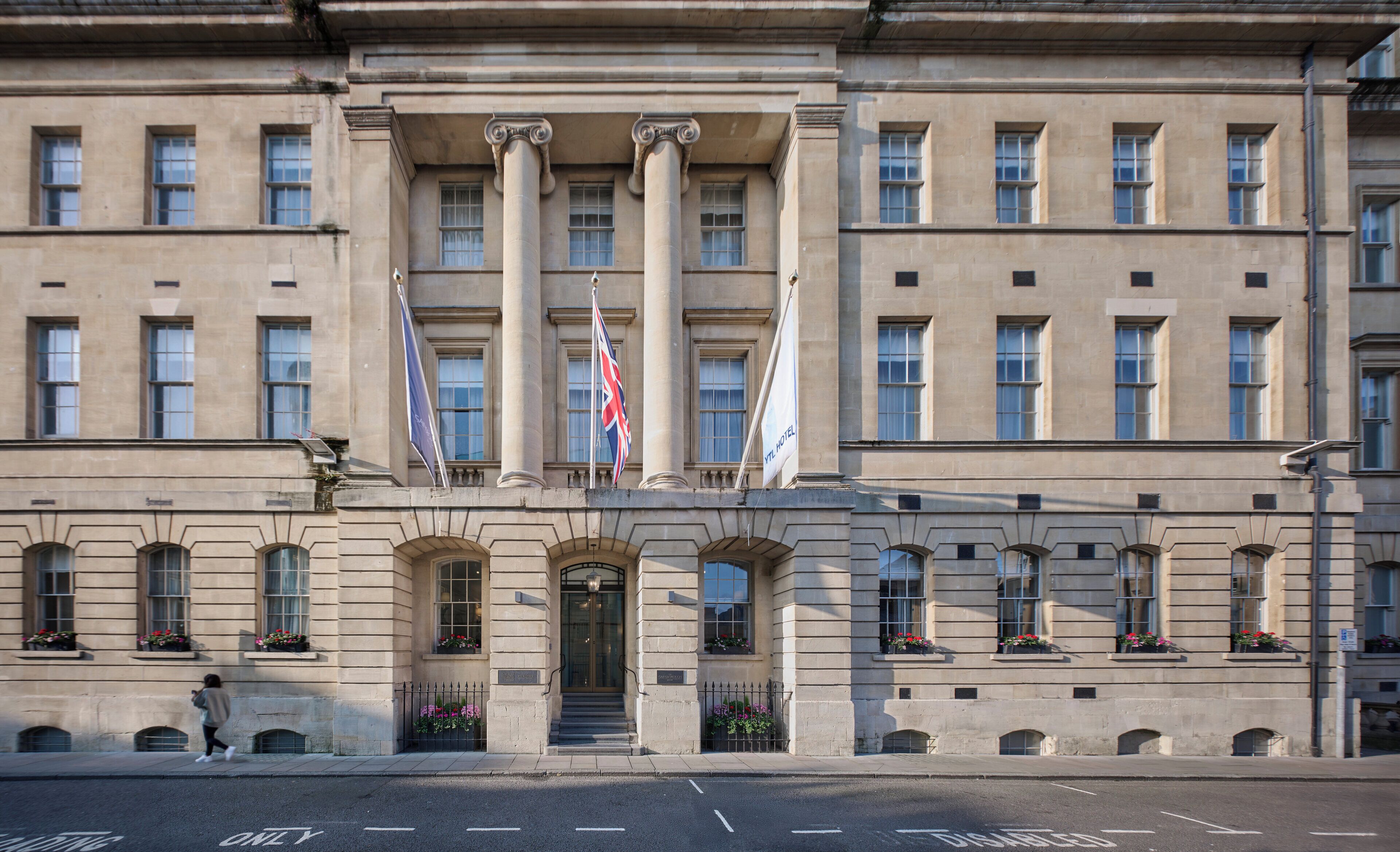 A large, classical building with multiple windows and columns, featuring flags and flower boxes.
