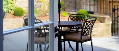 Un patio con mesa y sillas, una sombrilla y vistas a un edificio de piedra y vegetación.