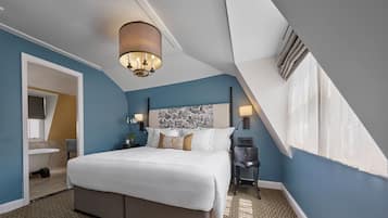 A bedroom with a large bed, a nightstand, a wall-mounted lamp, and a ceiling light fixture.